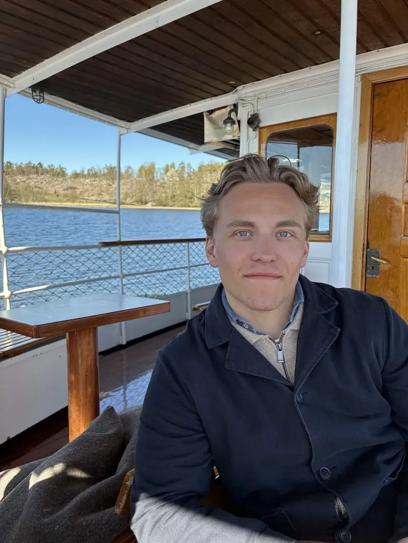 David Åkerlind smiling on the deck of a boat, with a lake and forest behind